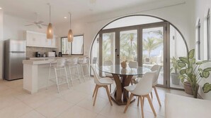 A modern kitchen with white cabinets, a stainless steel refrigerator, and a dining area with a glass table and white chairs. - Isla Mujeres Villa | Plunge Pool, Beach 90m & A/C (Isla Mujeres)