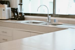 A kitchen with a white countertop, a sink, and a coffee maker.