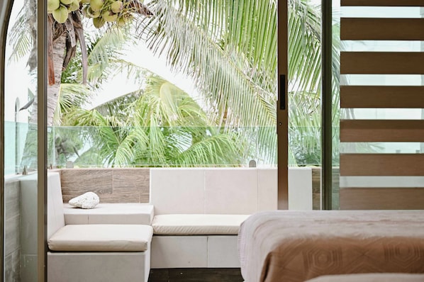 A room with a large window, a cushioned seating area, and a bed.