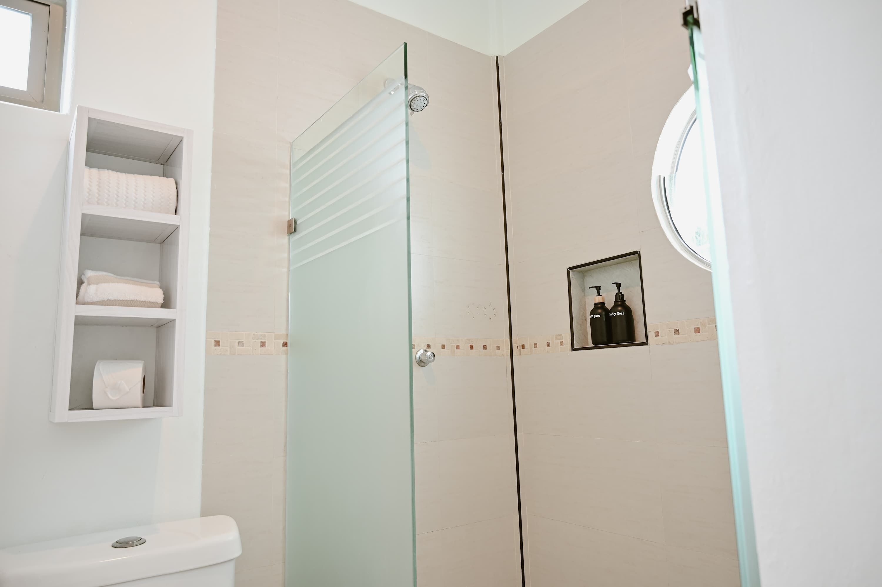 Un baño con cabina de ducha de vidrio, inodoro y estante con toallas.