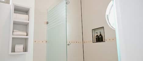 Un baño con cabina de ducha de vidrio, inodoro y estante con toallas.