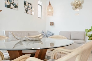 A modern living room with a glass table, wicker chairs, a sofa, and abstract wall art.