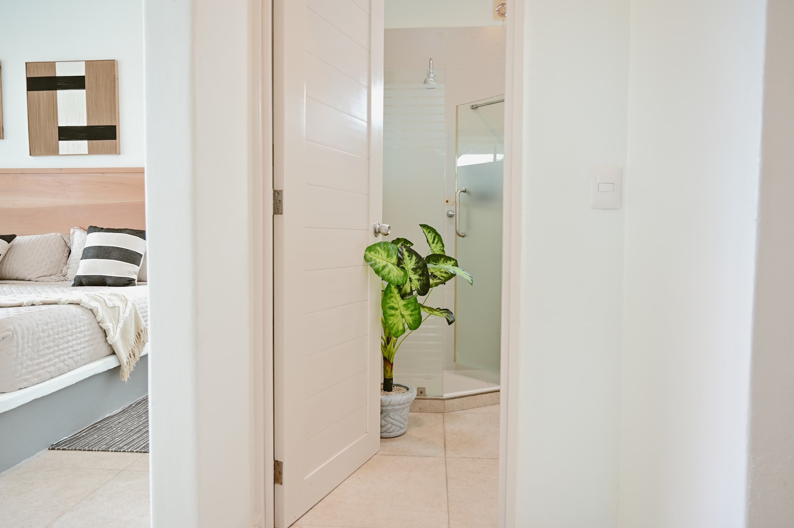 Ein Hotelzimmer mit Bett, Nachttisch, Blumentopf und Dusche.