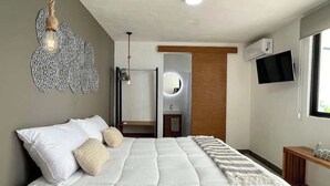 A bedroom with a bed, bedside table, TV, and a bathroom with a mirror and sink. - Downtown Cancun King Suite | Garden, WiFi & AC (CancÃºn)