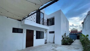 A modern building with a flat roof, a balcony with a metal railing, and a concrete ground. - Downtown Cancun King Suite | Garden, WiFi & AC (CancÃºn)