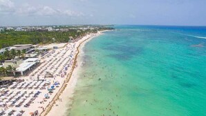 Une plage côtière bordée de rangées de transats et de parasols, une mer d’un bleu limpide et des bâtiments qui s’étendent le long du rivage.