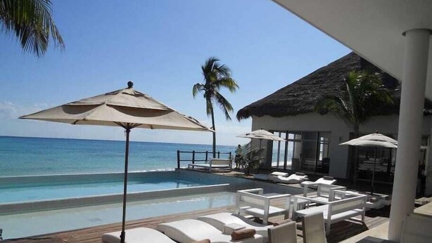 Un espace aménagé au bord de la piscine, avec des chaises longues et des parasols, une terrasse en bois et une vue sur l’océan.