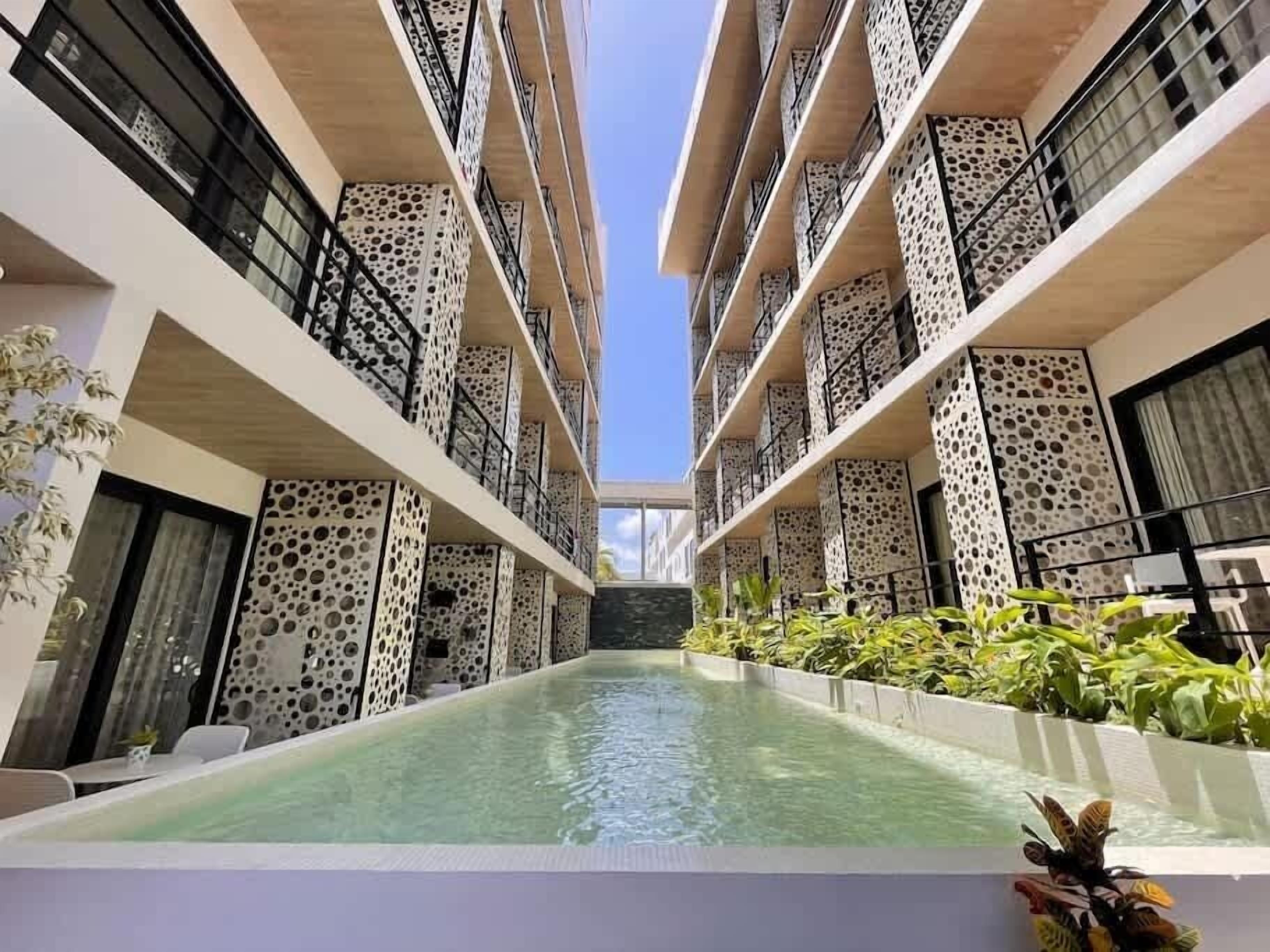 A modern building with a central pool, balconies with perforated patterns, and potted plants.