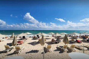 A beach with sun loungers and umbrellas, a clear sky, and the ocean in the background.