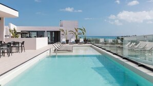 Ein Pool auf dem Dach mit Liegestühlen, einer Sitzecke und Blick aufs Meer.