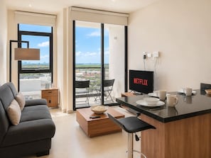 A modern living room with a sofa, a coffee table with a bowl of popcorn, a TV displaying 'NETFLIX', and a balcony with a view of the city.