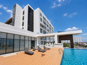 A modern hotel with a rooftop pool, sun loungers, and a clear view of the city skyline.