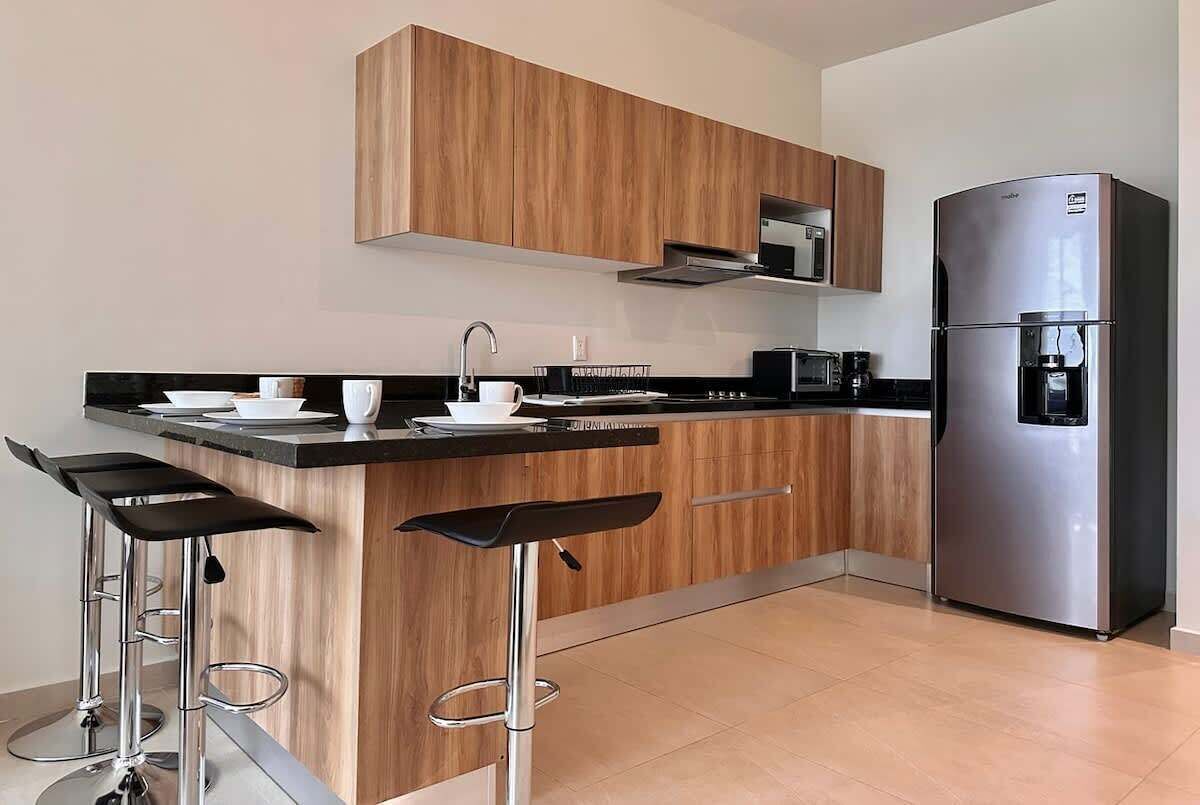 A modern kitchen with wooden cabinets, a stainless steel refrigerator, a microwave, and two bar stools.