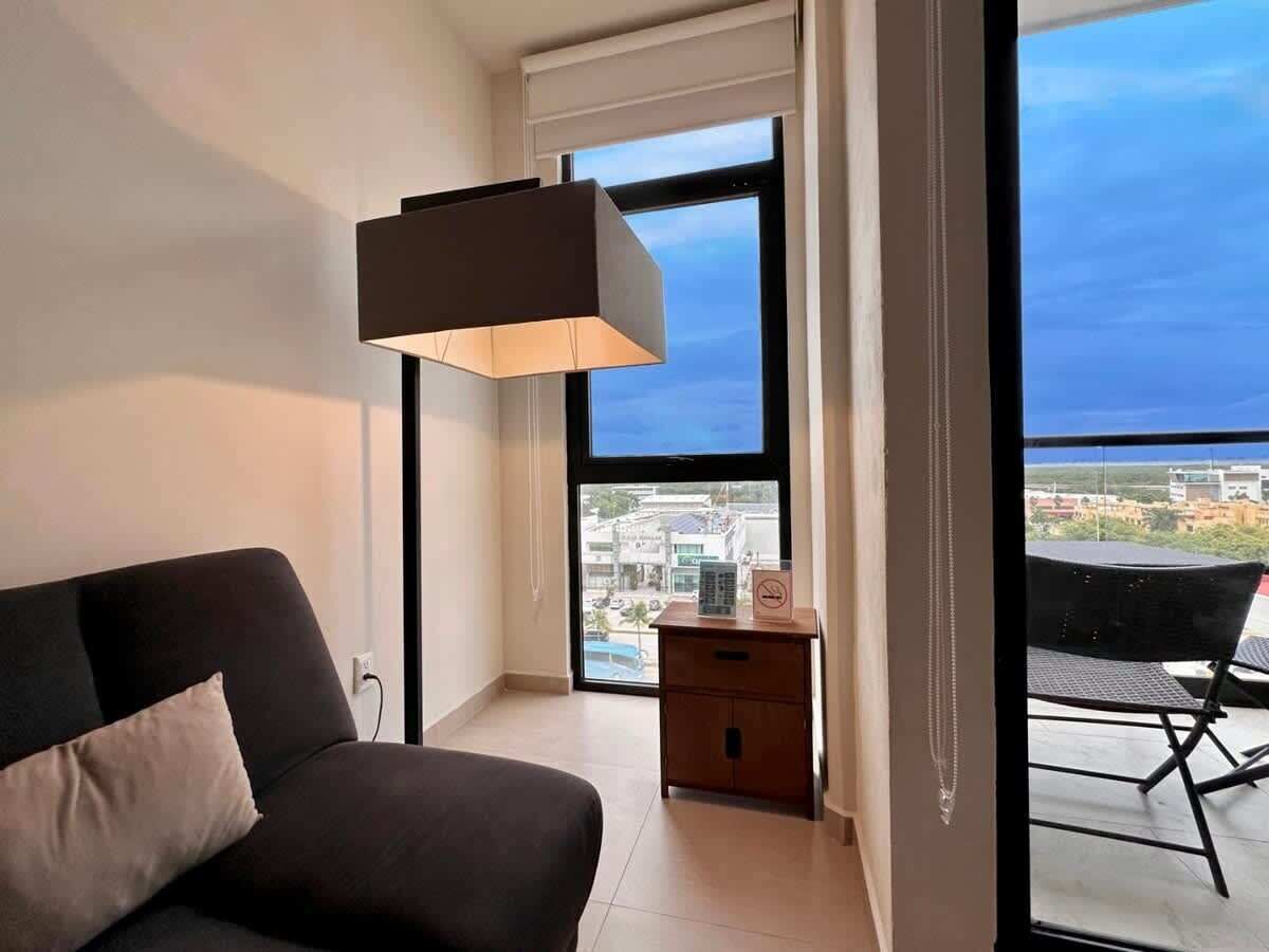 Une chambre moderne avec un canapé, un petit meuble en bois et une grande fenêtre donnant sur la ville.