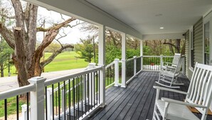 A covered porch with white railings, wooden deck, and white rocking chairs.