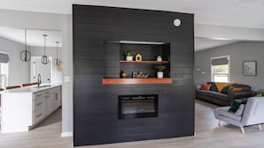 A modern living room with a black accent wall, a built-in fireplace, and wooden shelves with decorative items.