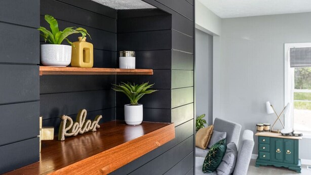 A modern living room with a dark wall, wooden shelves, and a green side table.