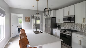 A modern kitchen with white cabinetry, stainless steel appliances, and pendant lighting.