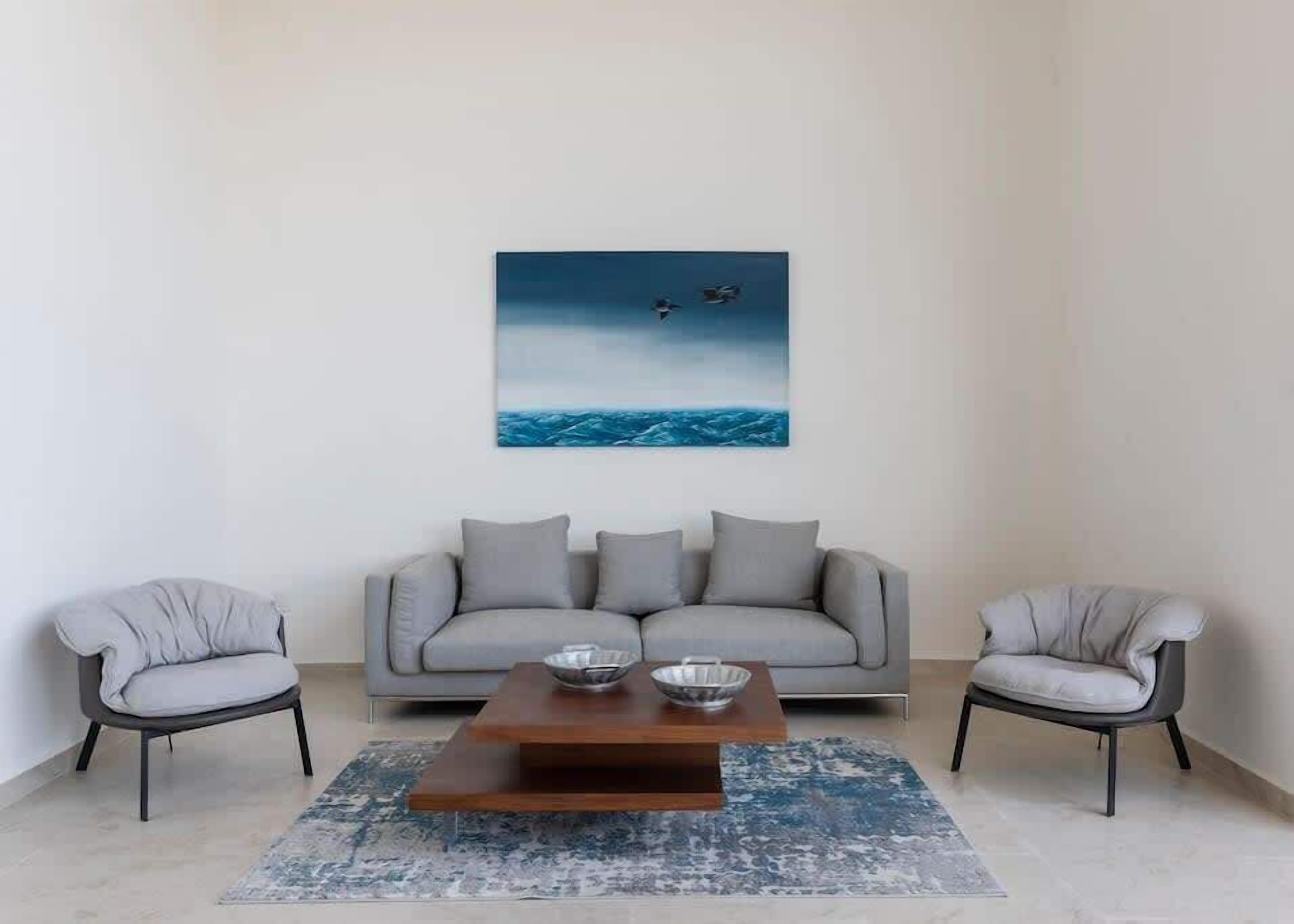 A living room with a sofa, two armchairs, a coffee table, and a painting of birds over water.
