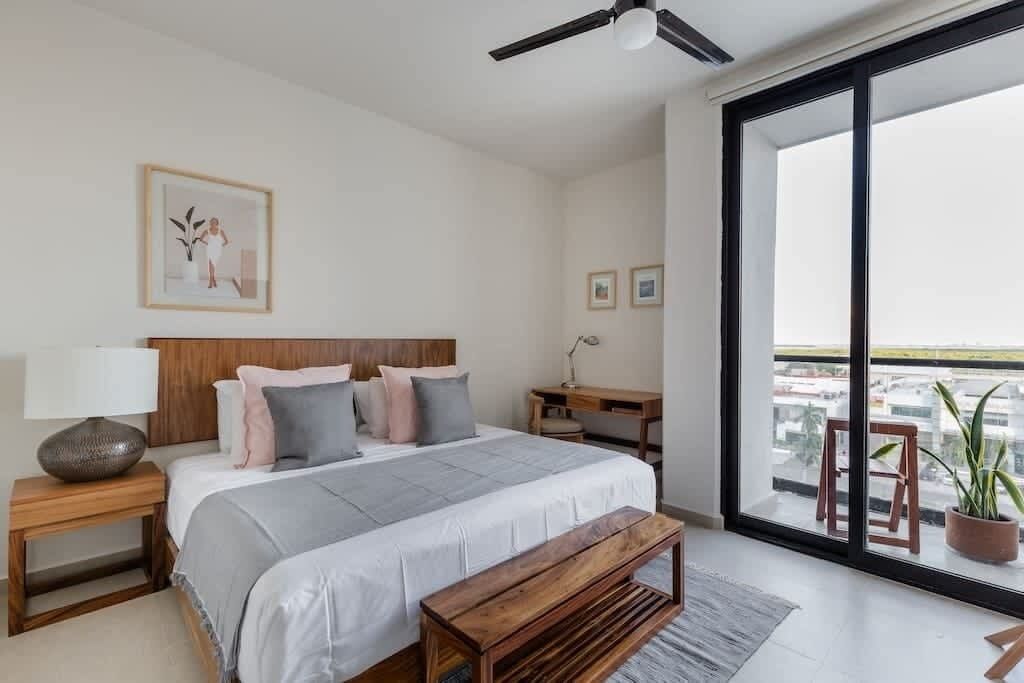 A bedroom with a bed, bedside tables, a bench, a desk, and a large window with a view.