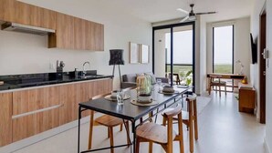 A modern kitchen with wooden cabinets, a black countertop, and a dining area with a table and chairs. - Cancun 1BR | Lagoon View, Pool & Gym | SF 801 (CancÃºn)