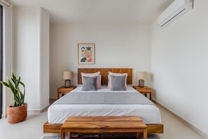 Ein modernes Schlafzimmer mit einem hölzernen Bett, zwei Nachttischen mit Lampen, einer Zimmerpflanze und einem gerahmten Bild an der Wand.