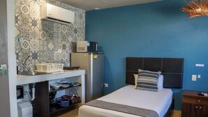 A bedroom with a bed, a nightstand, a dresser, a built-in shelf with kitchen items, and a wall-mounted air conditioner. - Central Studio + Rooftop, Downtown Cancun (Cancún)