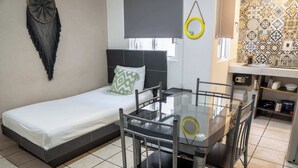 A compact room with a single bed, a small table with chairs, a kitchen area with a sink and storage, and a patterned wall. - Cancun Central Studio: Rooftop Terrace & Kitchen (CancÃºn)
