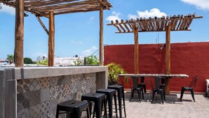 An outdoor bar area with a wooden pergola, tiled wall, and black stools. - Cancun Central Studio: Rooftop Terrace & Kitchen (CancÃºn)