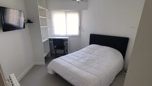 Ein Schlafzimmer mit Bett, Schreibtisch, Stuhl, Fernseher und Deckenleuchte.