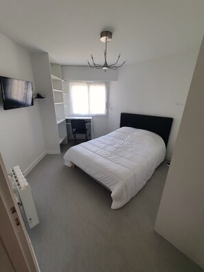 Un dormitorio con cama, escritorio, silla, televisor y lámpara en el techo.