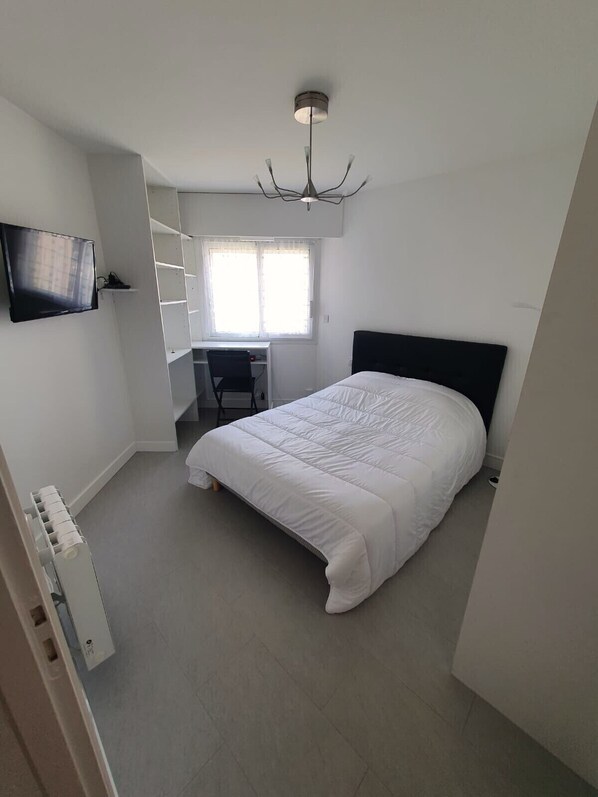 Ein Schlafzimmer mit Bett, Schreibtisch, Stuhl, Fernseher und Deckenleuchte.