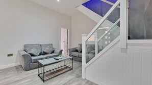 A modern living room with a grey sofa set, a coffee table, and a staircase with glass railings. - Dysa Waterloo Apartments (Blackpool)