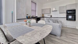 A modern kitchen with a dining area, featuring a large table with patterned placemats, a sofa, and a built-in oven. - Dysa Waterloo Apartments (Blackpool)