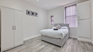 A bedroom with a bed, wardrobe, and a window with blinds. - Dysa Waterloo Apartments (Blackpool)