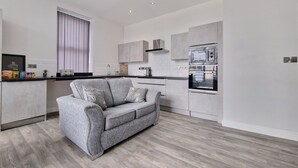 A modern kitchen with grey cabinetry, a built-in oven, and a grey sofa with cushions. - Dysa Waterloo Apartments (Blackpool)
