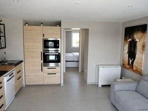 A modern kitchen with built-in appliances, a dining area with a white table, and a living room with a grey sofa. - Sol-y-Days la Darse, Apartment Marina Terrace view marina (Le Grau-du-Roi)
