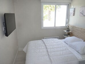 A bedroom with a bed, a TV mounted on the wall, a window, and a bedside table with a lamp. - Sol-y-Days la Darse, Apartment Marina Terrace view marina (Le Grau-du-Roi)