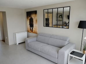 Una sala de estar moderna con un sofá gris, un espejo grande, un radiador y una mesita con un control remoto.