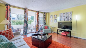 Una sala de estar con sofá, mesa de centro, televisor y vistas amplias a través de grandes ventanales.