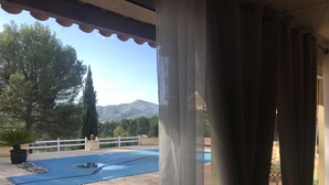 A covered outdoor area with a pool, a white fence, and a view of trees and mountains. - In a quiet, hilly setting, bright residence under the pine trees! (La Bouilladisse)