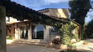 A house with a tiled roof, large windows, and a covered porch area with potted plants. - In a quiet, hilly setting, bright residence under the pine trees! (La Bouilladisse)
