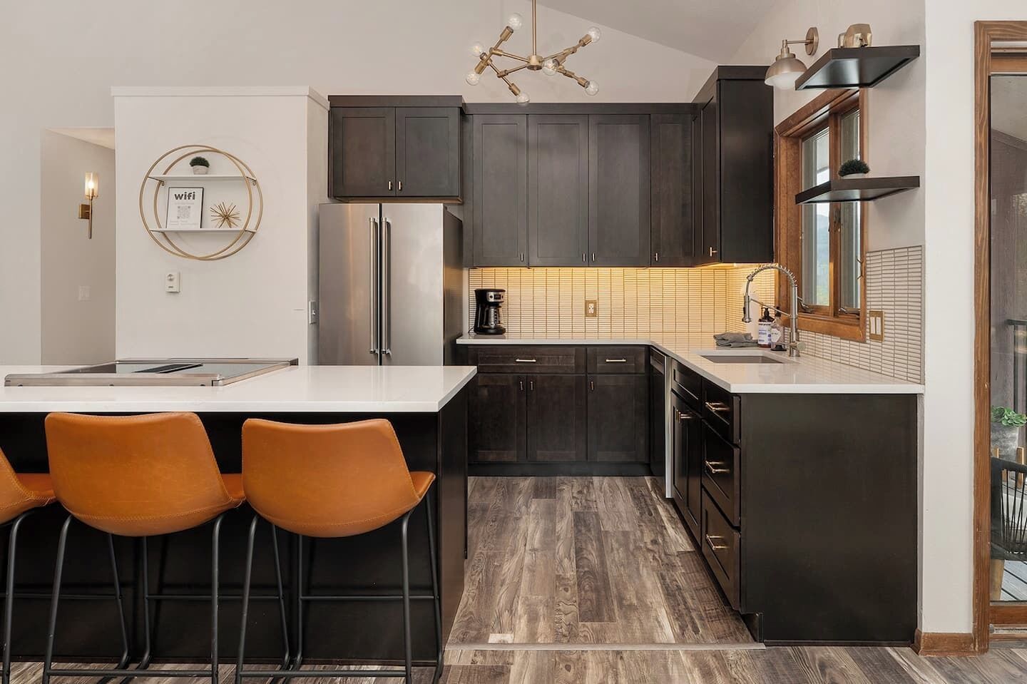A modern kitchen with dark cabinets, a stainless steel refrigerator, a coffee maker, and a bar area with stools.