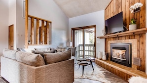 A cozy living room with a fireplace, a large sofa, and a television. - Amazing Views! Downtown Penthouse with Sauna (Winter Park)