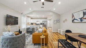 A modern living room with a sofa, a dining table, and a kitchen in the background. - Tranquil TU Getaway! EXPO/Route 66/Cherry St -3bd (Tulsa)