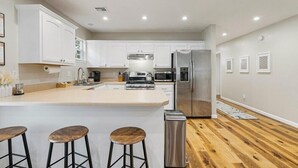 A modern kitchen with white cabinets, a central island with stools, stainless steel appliances, and wooden flooring. - Tranquil TU Getaway! EXPO/Route 66/Cherry St -3bd (Tulsa)