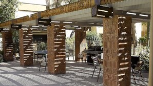 Ein Außenbereich mit Terrasse, Säulen mit Muster, einem Grill und einer Sitzecke.