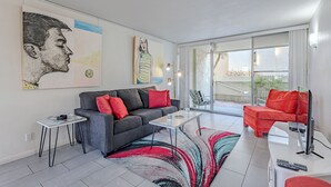 Ein modernes Wohnzimmer mit grauem Sofa, roten Kissen, einem Glastisch und Kunstwerken an der Wand.