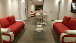 Un hall d’hôtel moderne avec des canapés rouges et blancs, une table basse en verre et un coin repas avec des chaises et une table blanches.