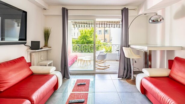 Un salon moderne avec des canapés en cuir rouge, une table basse en verre et un balcon offrant une vue sur les immeubles et la verdure.